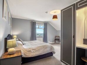 Une chambre à coucher avec un lit, une table de chevet, une lampe, une chaise et une vue sur la mer par la fenêtre.