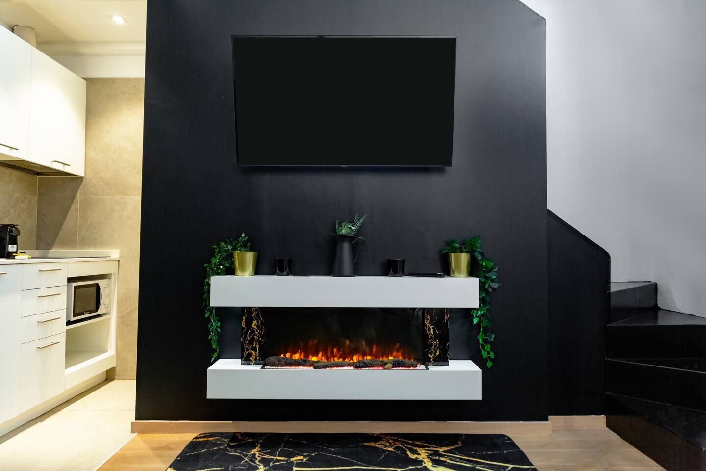 A modern living room with a fireplace, a mounted TV, and a kitchen area with a microwave.