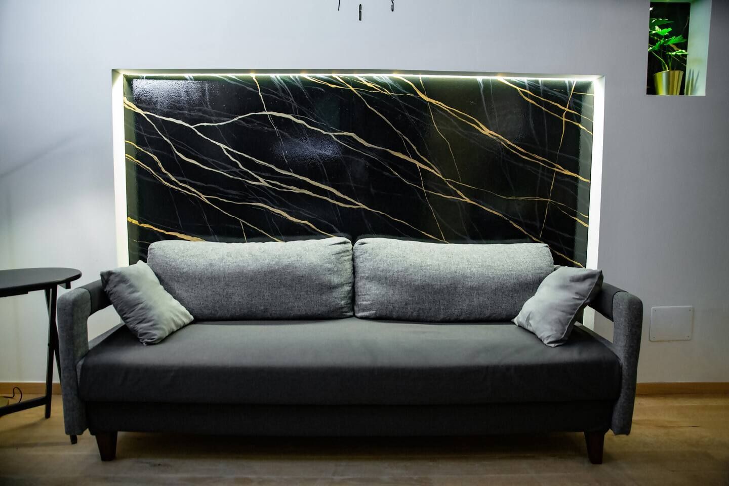 Ein modernes Wohnzimmer mit einem grauen Sofa, zwei grauen Kissen und einer Wand mit einem schwarzen und goldenen abstrakten Design.