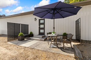 Un patio con mesa y sillas, un paraguas grande y una puerta con ventanas.