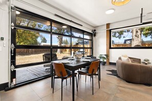 A modern dining area with a large window, a dining table with chairs, and a sofa. - The Back Nine | King Bed, Fireplace & Fenced Yard (Fort Collins)