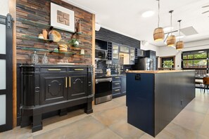 A modern kitchen with dark cabinetry, a central island, and a rustic wall design. - The Back Nine | King Bed, Fireplace & Fenced Yard (Fort Collins)