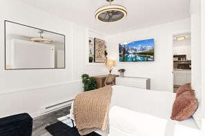 Ett modernt sovrum med en säng, ett nattduksbord, en lampa och en tavla som föreställer ett berglandskap.
