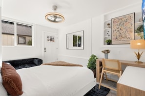 Ein modernes Schlafzimmer mit Bett, Schreibtisch, Stuhl, Fenster und Deckenventilator.