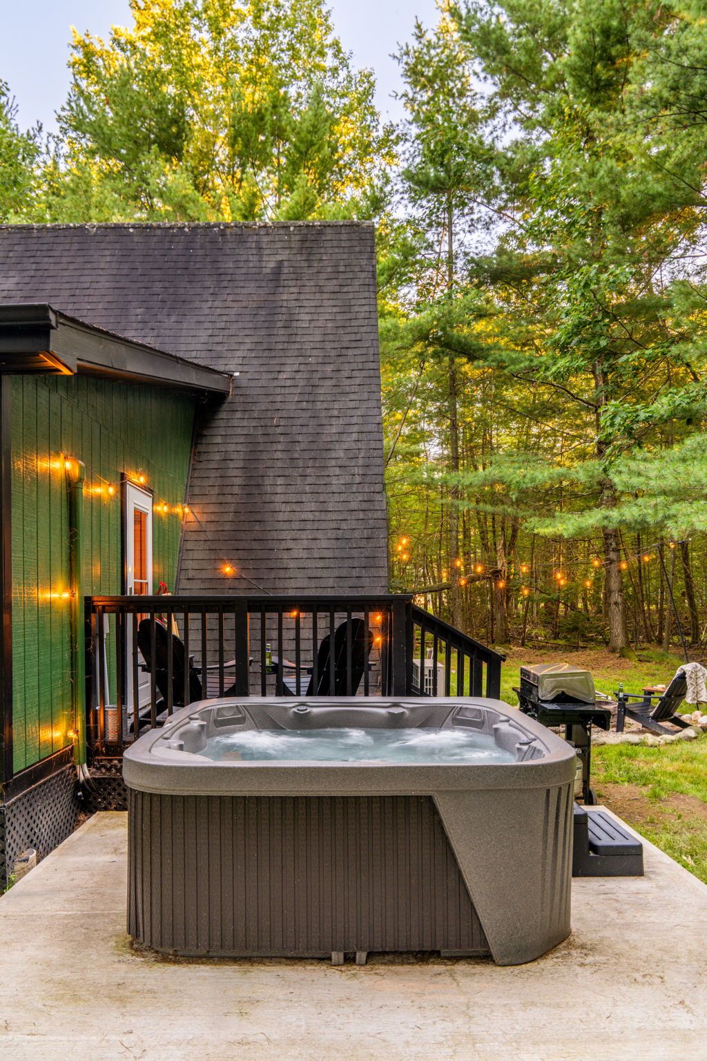 Un jacuzzi dans un jardin, avec une terrasse en bois et un bâtiment en arrière-plan.