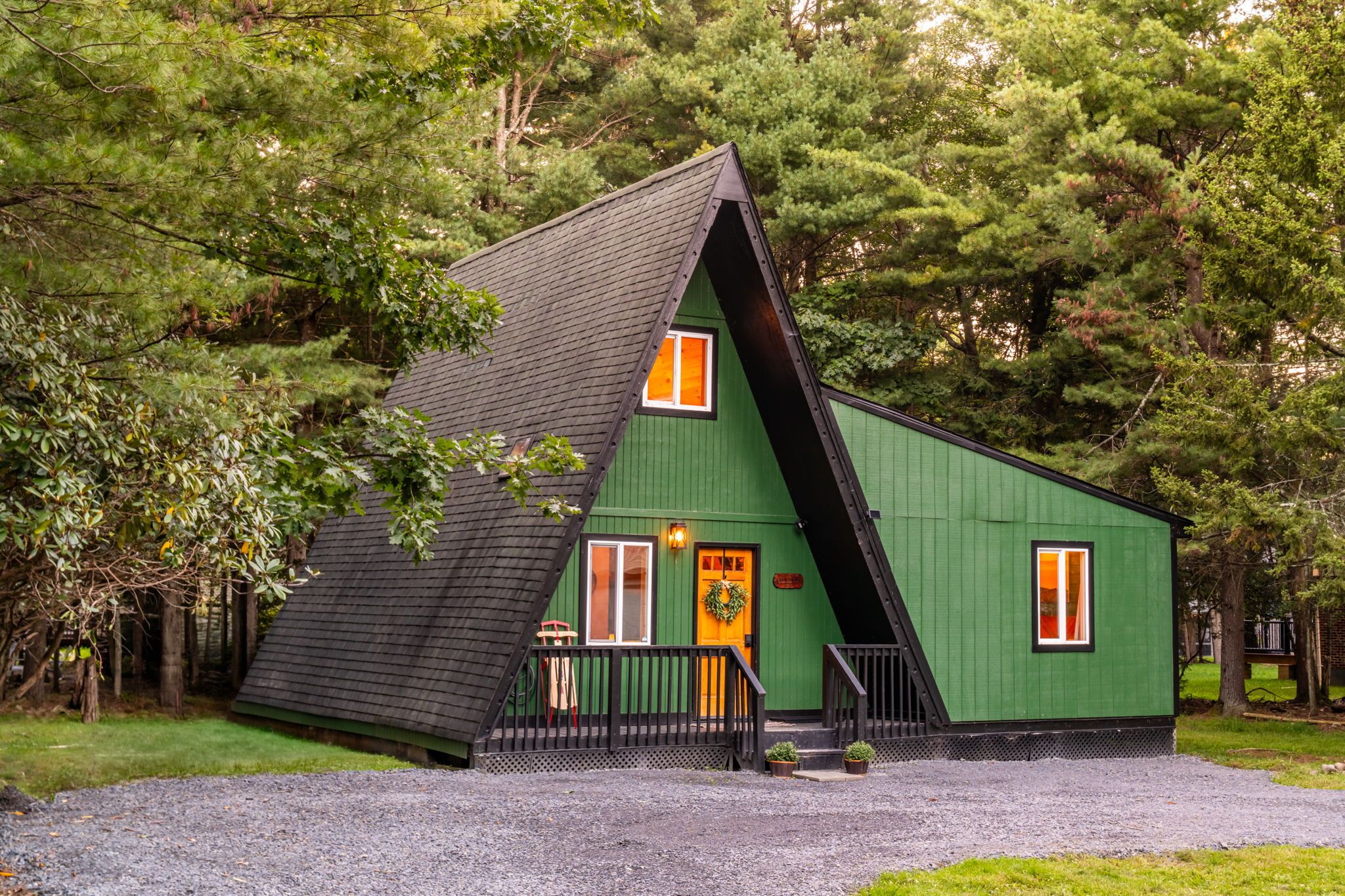 A green building with a sloped roof, a front porch, and a door with a wreath.