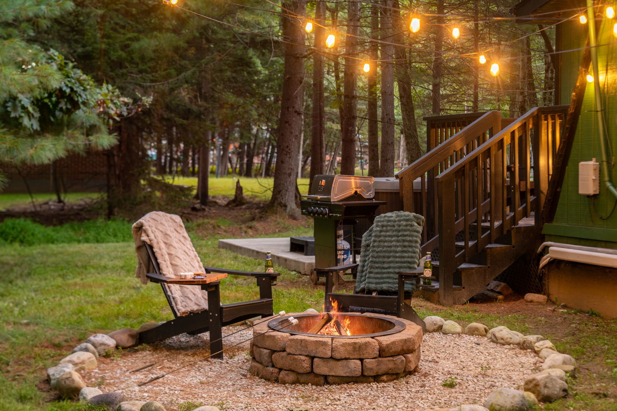 A cozy outdoor seating area with a fire pit, a chair with a blanket, and a staircase leading to a covered deck.