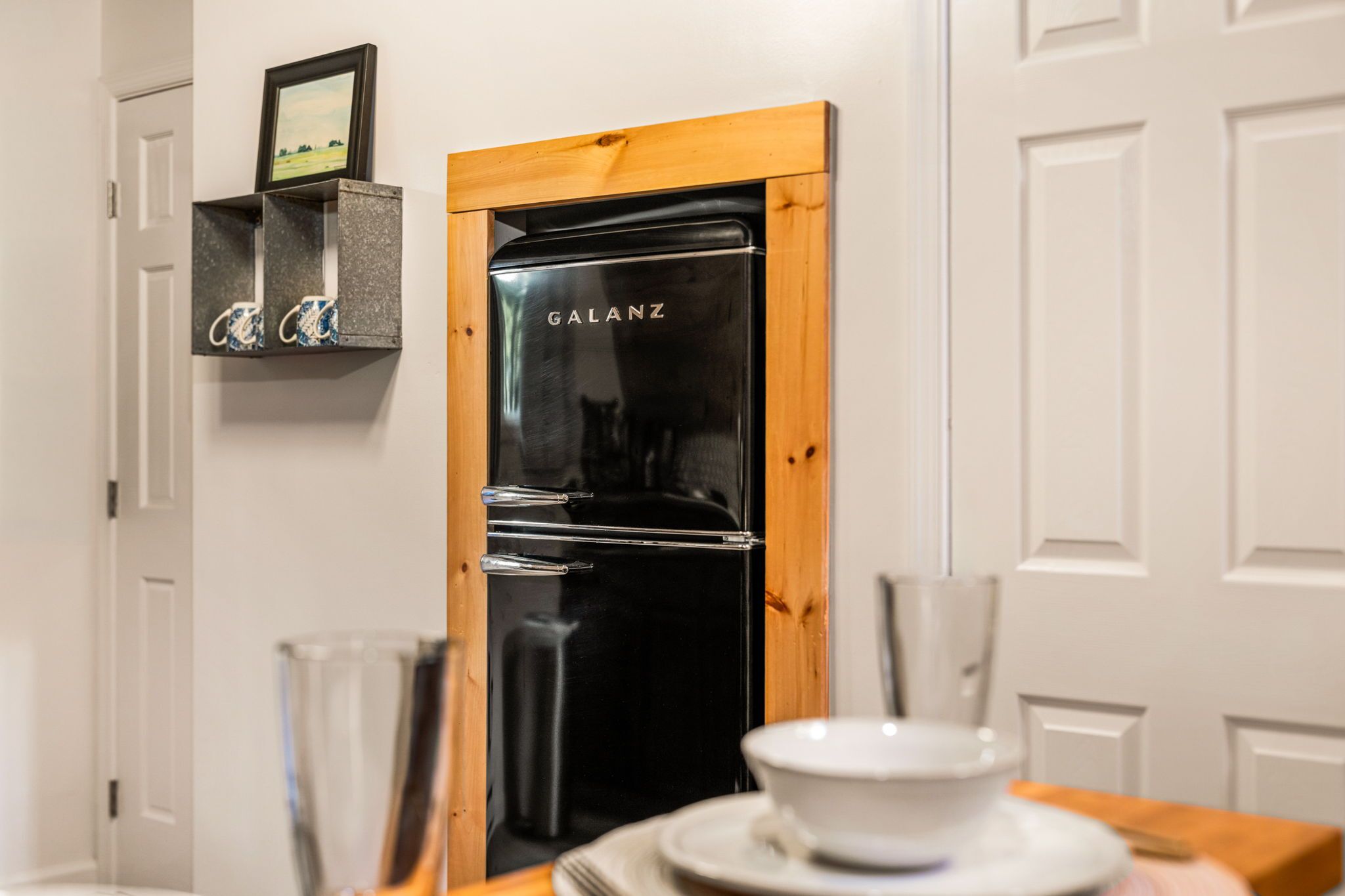 A modern kitchen with a black refrigerator, wooden frame, and a white door.