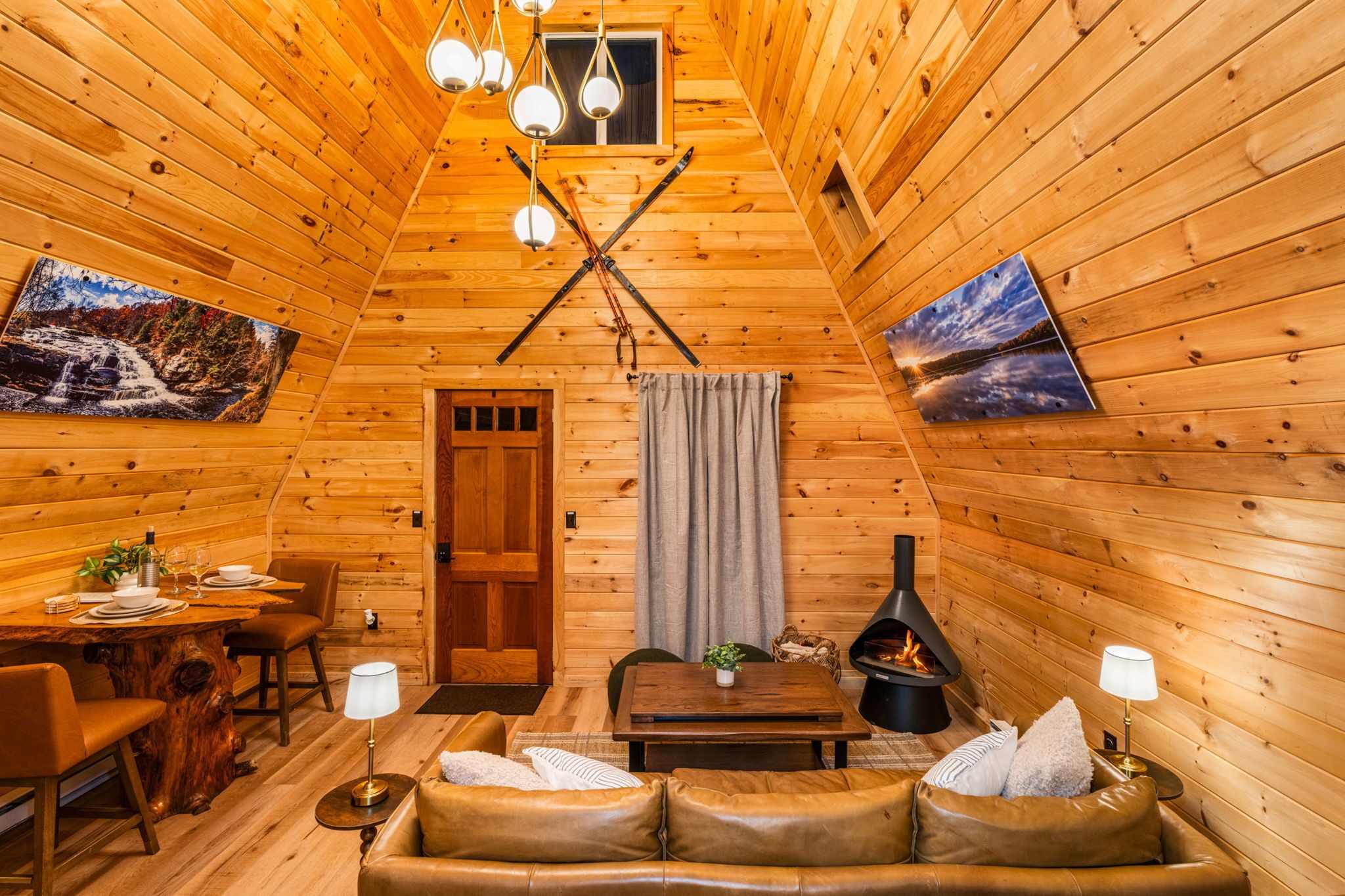 A cozy cabin interior with wooden walls, a dining area, a sofa, and a fireplace.