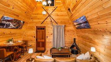 A cozy cabin interior with wooden walls, a dining area, a sofa, and a fireplace.