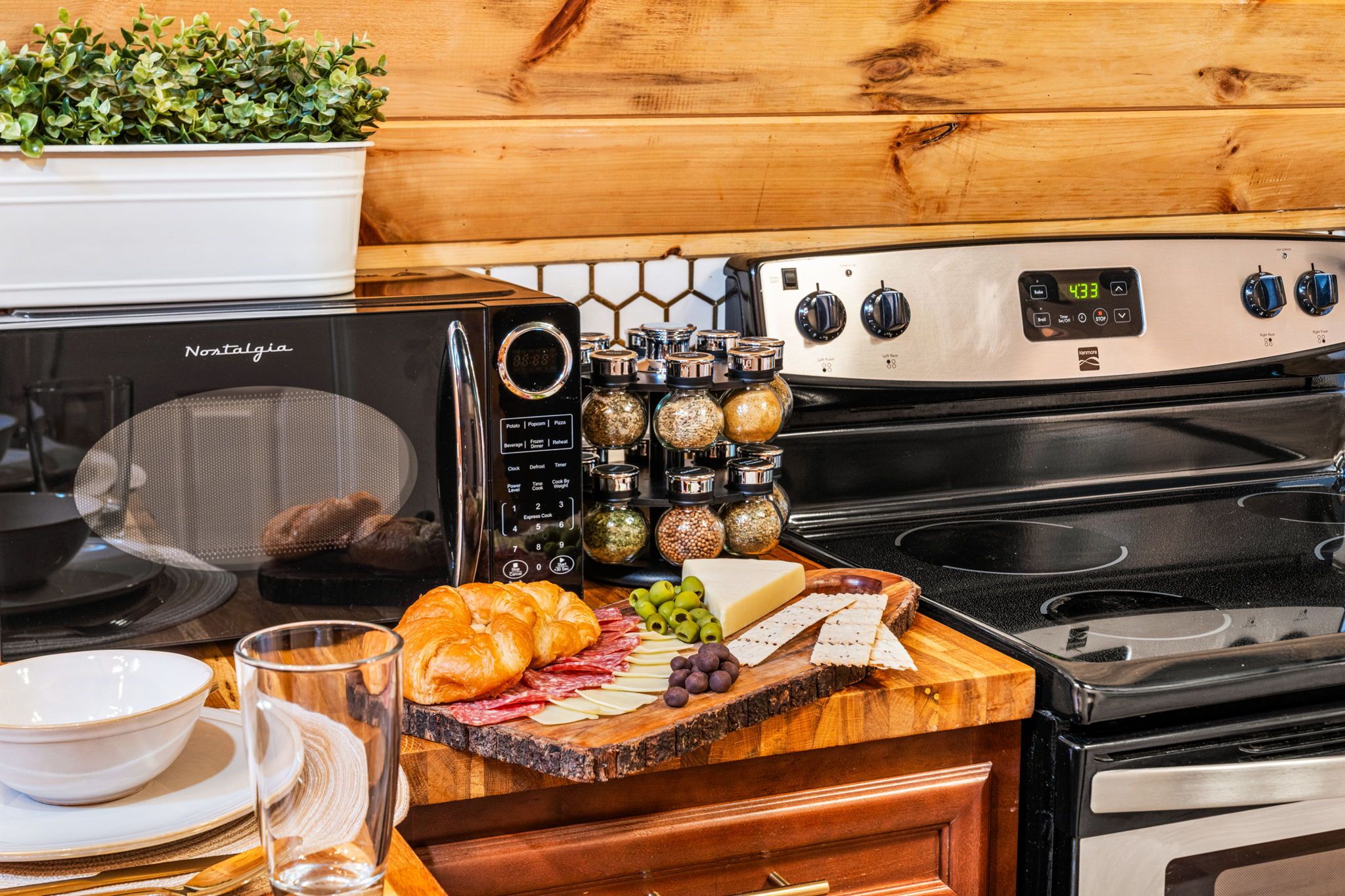 Une cuisine équipée d’un four à micro-ondes de la marque Nostalgia, d’une planche à découper en bois avec des aliments, et d’une cuisinière.