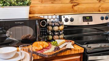 Une cuisine équipée d’un four à micro-ondes de la marque Nostalgia, d’une planche à découper en bois avec des aliments, et d’une cuisinière.