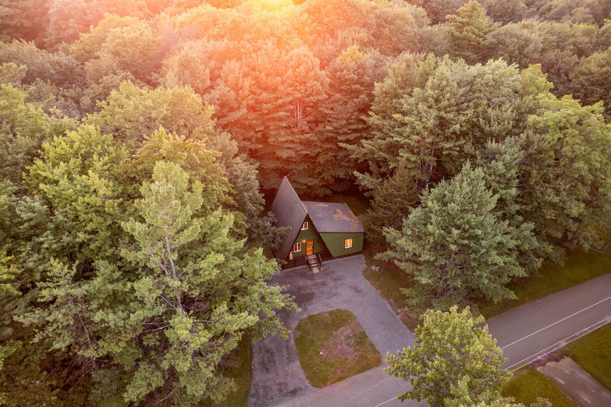 A cabin surrounded by dense forest with a gravel driveway leading to the entrance.
