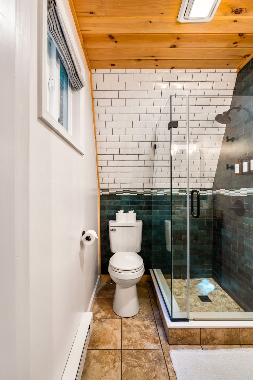 Une salle de bain avec des toilettes blanches, une douche en verre et un mur carrelé.