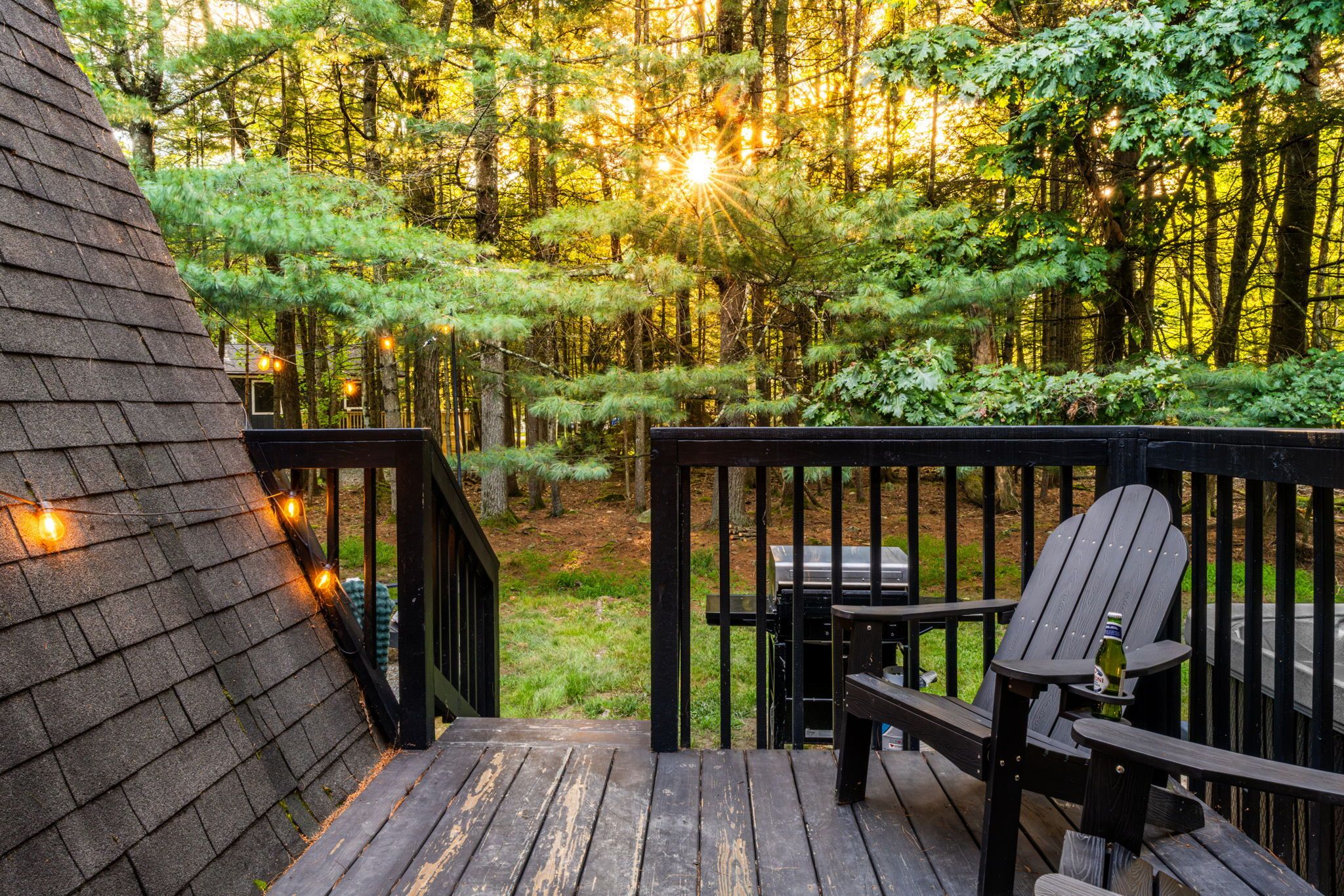 A wooden deck with a grill and seating area, surrounded by a forest.