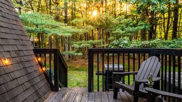 A wooden deck with a grill and seating area, surrounded by a forest.
