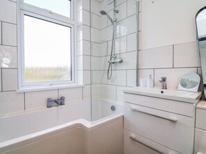 A modern bathroom with a bathtub, a glass-enclosed shower, a window, and a vanity with a mirror. - 29 Brynford (Ellesmere Port)