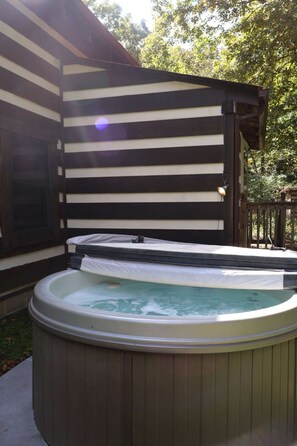 A hot tub in a covered outdoor area with a wooden deck and a house in the background. - Cozy cabin with mini arcade games hot tub and fire pit (Logan)