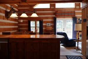 Ein rustikales Blockhaus-Interieur mit einem Holzespeisesaal, Stühlen, einem Kamin und einem großen Fenster.