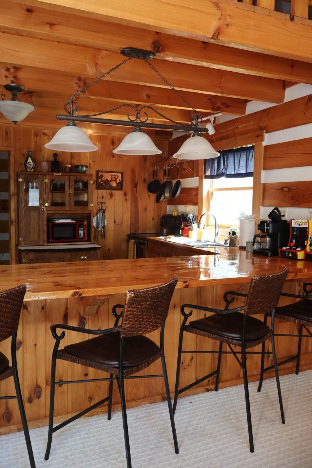 A wooden interior with a bar area, chairs, a microwave, and hanging pans.