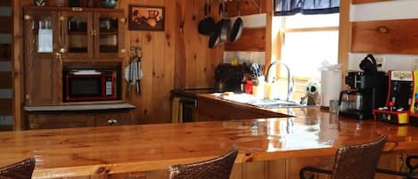 A wooden interior with a bar area, chairs, a microwave, and hanging pans.