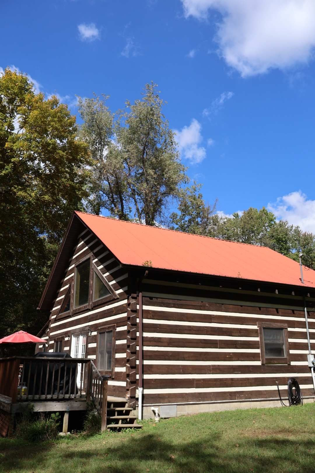 A log cabin with a red roof, a porch, and a window.