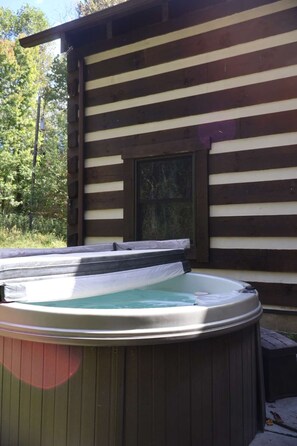Ein Whirlpool vor einer Holzhütte mit einem Fenster.