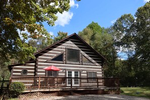 A log cabin with a deck, a red umbrella, and a large window. - Cozy cabin with mini arcade games hot tub and fire pit (Logan)