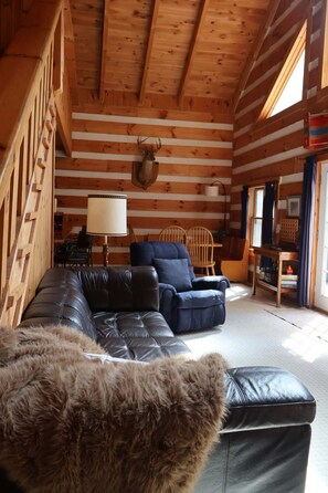 A log cabin interior with a leather sofa, a mounted deer head, and a wooden table. - Cozy cabin with mini arcade games hot tub and fire pit (Logan)