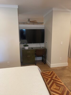 Ein Schlafzimmer mit einem Bett, einem Schreibtisch mit Stuhl, einem Fernseher und einem Deckenventilator.