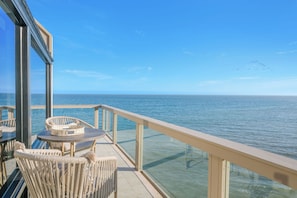 Ein Balkon mit Meerblick, Korbmöbel und einer Glasreling.