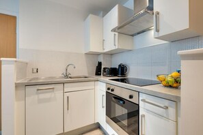 Eine moderne Küche mit weißen Schränken, einer Edelstahl-Spüle, einer schwarzen Kaffeemaschine und einer Obstschale auf der Arbeitsplatte.