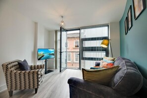 Ein modernes Wohnzimmer mit einer Couch, einem Sessel, einem Fernseher und Blick durch eine Glastür.