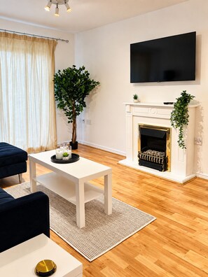 Ein modernes Wohnzimmer mit Fernseher, Kamin, Esstisch und einer Couch.