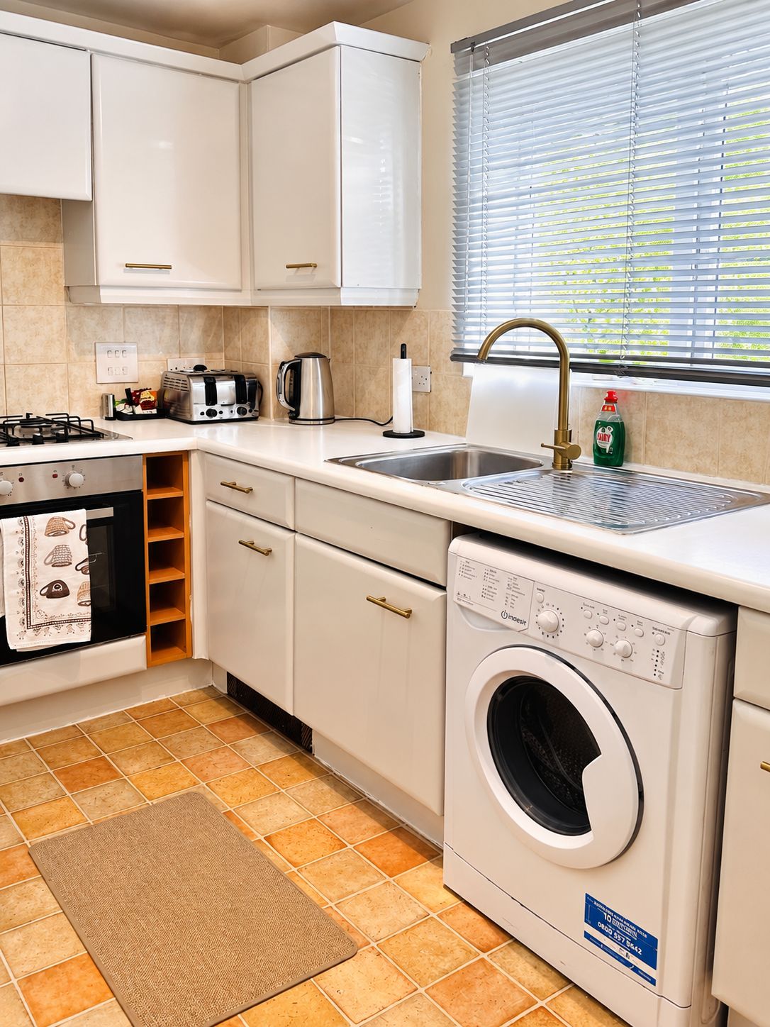 A kitchen with white cabinets, a built-in washing machine, a gas stove, and a window with blinds.
