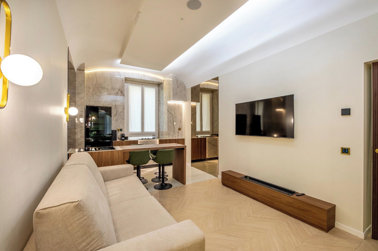 Una sala de estar moderna con un sofá, un televisor montado en la pared y una cocina con salpicadero de mármol.
