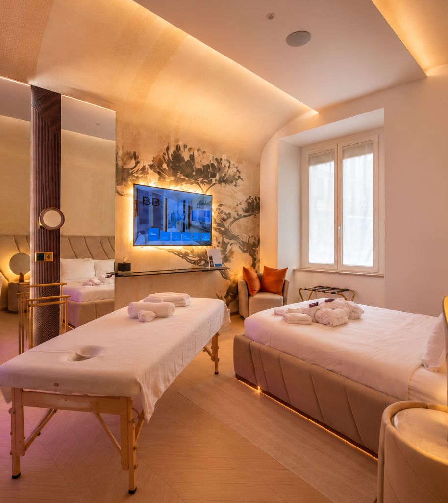 Habitación de hotel con dos camas, una camilla de masaje, un televisor y una ventana.