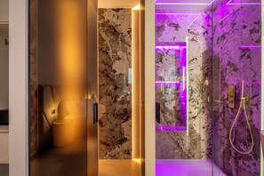 A modern bathroom with a marble wall, a shower with a golden showerhead, and a glass partition. - Borghese Boutique (Rome)