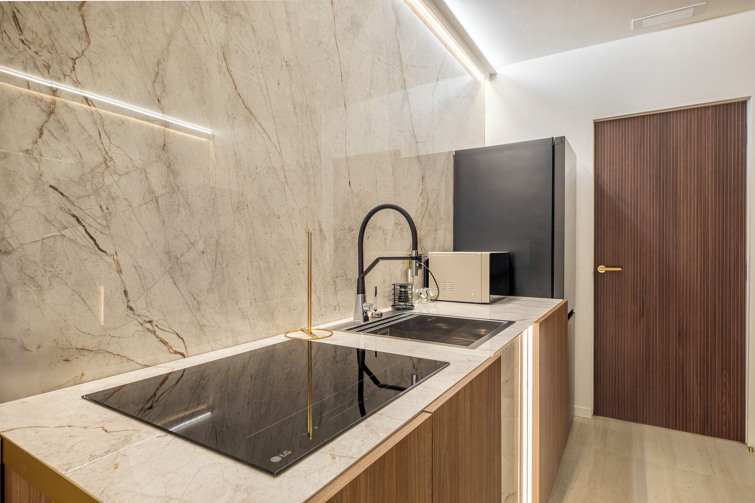 A modern kitchen with a marble backsplash, a black induction cooktop, and wooden cabinetry.