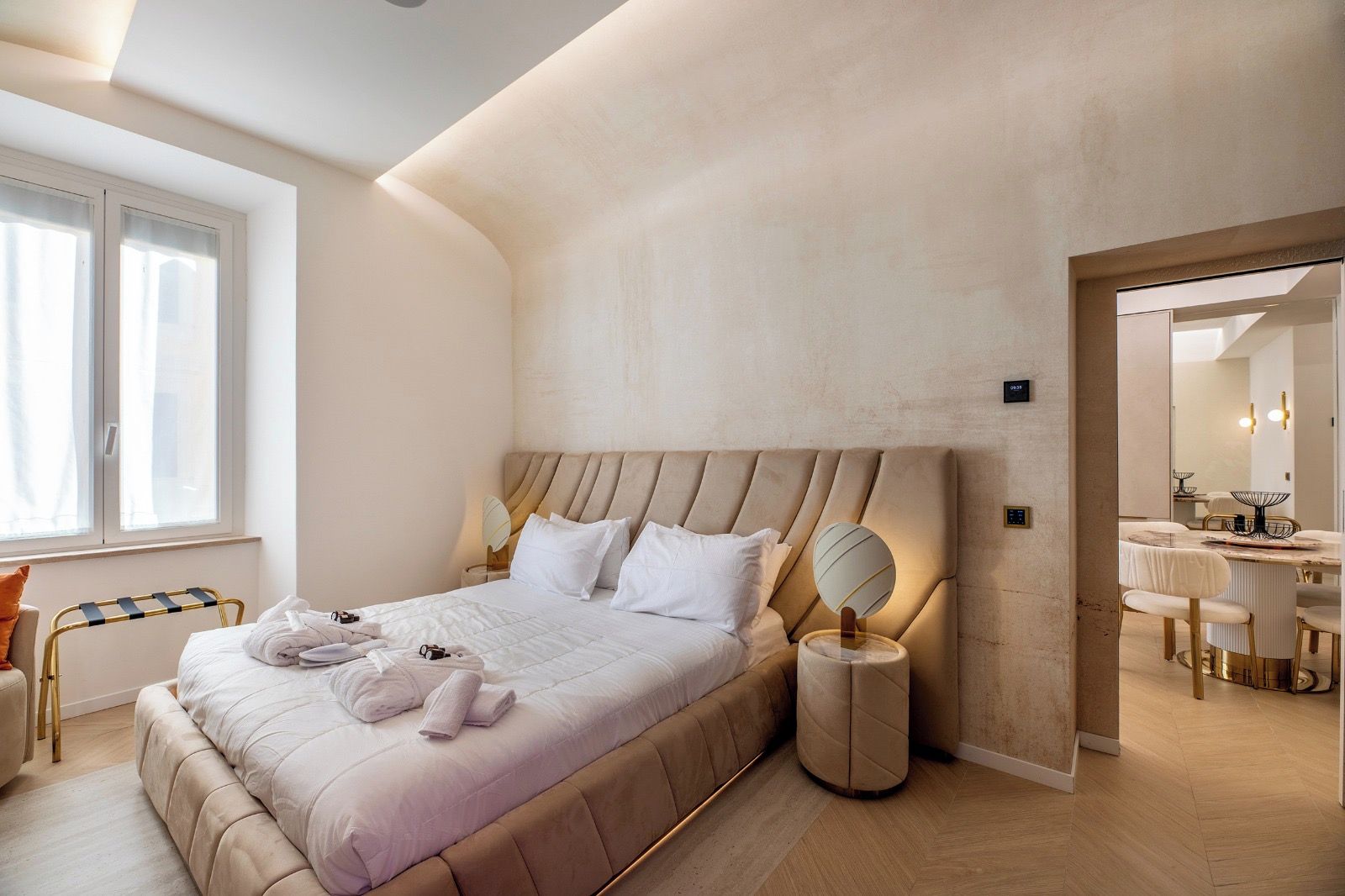Habitación de hotel moderna con una cama grande, lámparas de noche, un espejo y vistas al comedor.