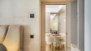 Une chambre d’hôtel comprenant un lit, une table de chevet, une horloge murale et une porte donnant sur un coin repas avec une table et des chaises.