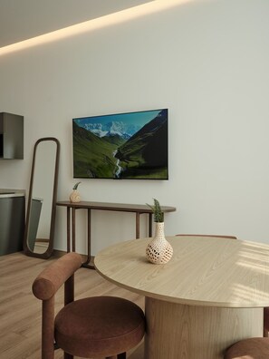 A modern dining area with a round wooden table, two brown cushioned chairs, a decorative vase, and a framed landscape painting on the wall. - Roma Residence | Luxury Suite 204 (Mexico City)