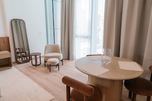 A modern hotel room with a round wooden dining table, two chairs, a round mirror, and a large window with curtains. - Roma Residence | Luxury Suite 201 (Mexico City)