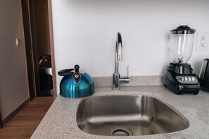 Ett kök med en diskho i rostfritt stål, en blå vattenkokare, en modern blandare och en svart matberedare på bänkskivan.