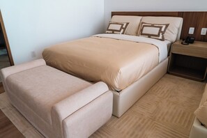 Un lit avec un banc assorti, une table de chevet avec un téléphone et une prise électrique sur le mur.