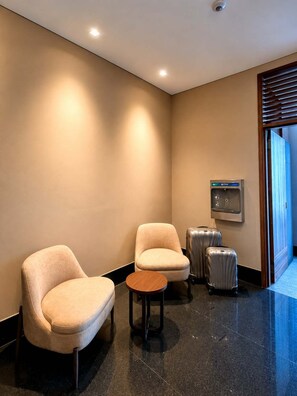 Un hall d’hôtel avec deux fauteuils, une petite table ronde et un chariot à bagages.