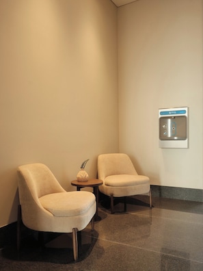 A seating area with two chairs and a small table, a wall-mounted water dispenser, and a textured floor. - Condesa Residence - Roma Luxury Suite 505 (Mexico City)