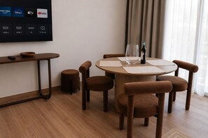 A modern hotel room with a round dining table, four upholstered chairs, a wooden side table, and a flat-screen TV displaying streaming services. - Roma Residence | Luxury Suite 203 (Mexico City)