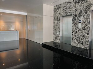 A modern elevator with a granite wall, a glass elevator door, and a control panel. - Roma Residence | Luxury Suite 203 (Mexico City)