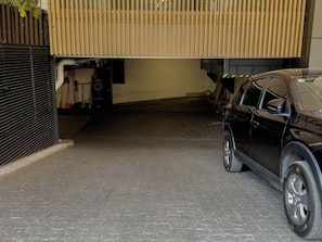 Área de estacionamento com um SUV preto, uma porta de garagem fechada e um edifício com design de ripas verticais de madeira.